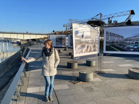 Žena pored rijeke (Dunav). U pozadini plakati grada Beograda uz vodu.