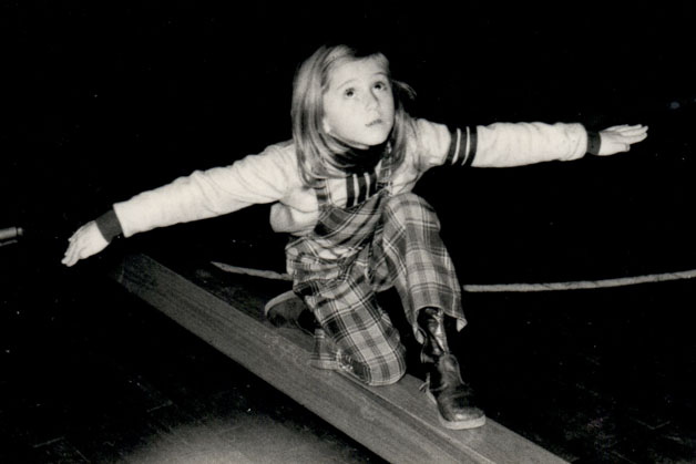 Ein Mädchen in Stiefeln und karierter Hose mit Knie auf einem Sportbrett hält ihr Gleichgewicht