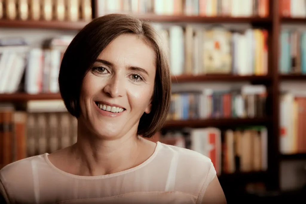 Lächelndes Gesicht einer Frau, unscharfe Bücherregale im Hintergrund