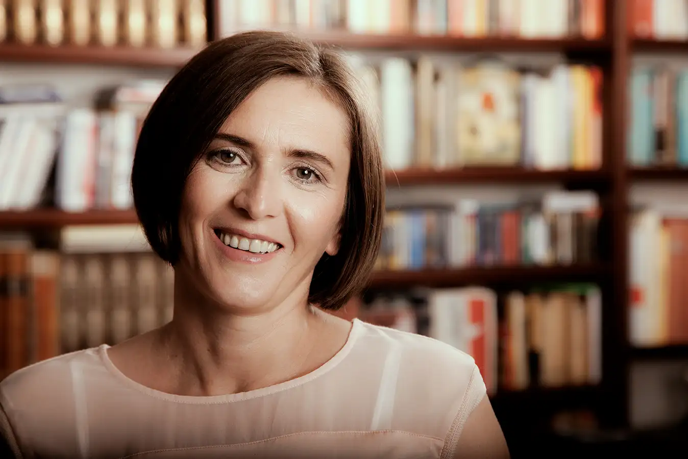 Lächelndes Gesicht einer Frau, unscharfe Bücherregale im Hintergrund